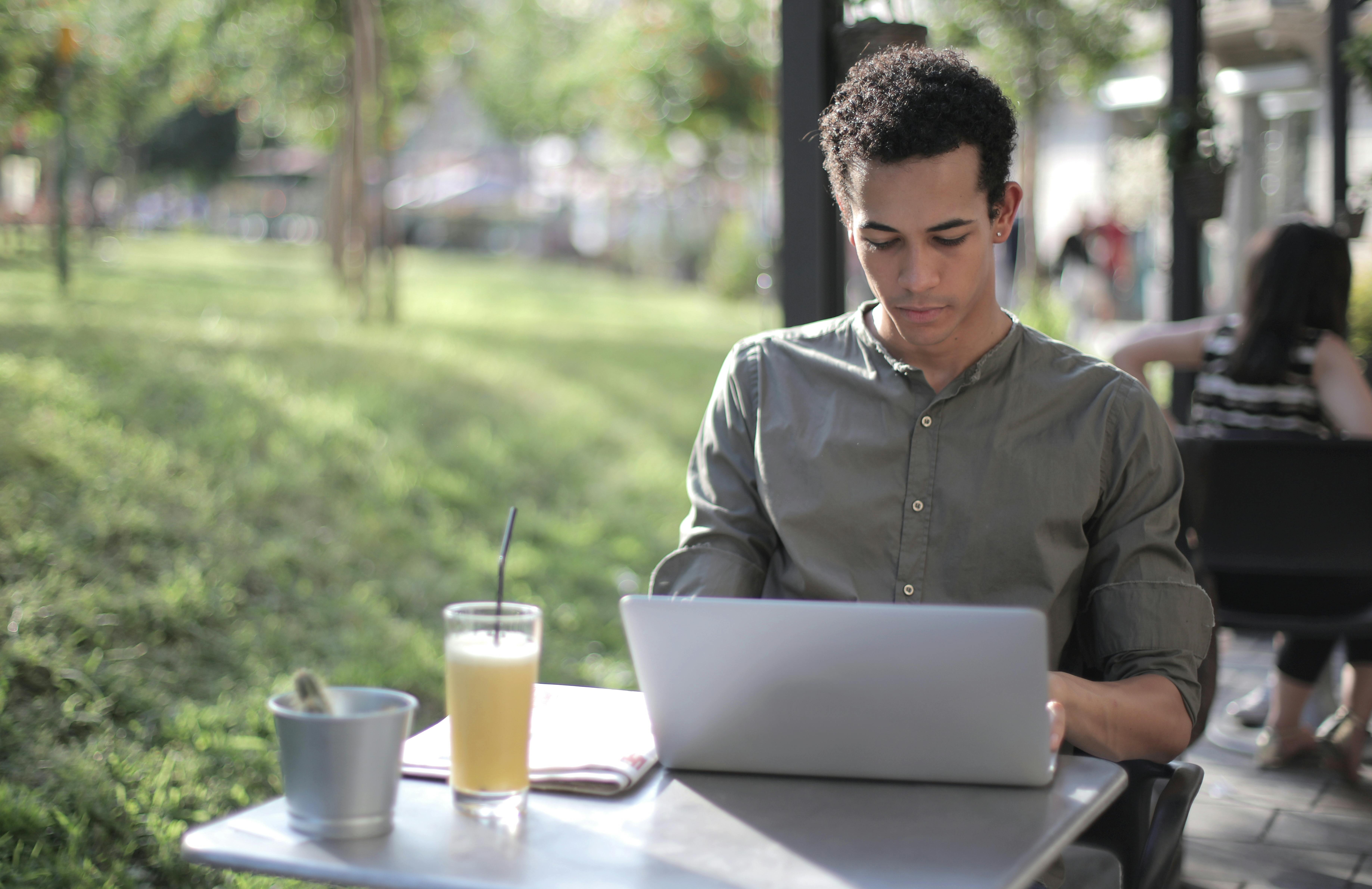male law student at an outdoor cafe wearing a law school attire of grey button-down shirt, sleeves folded at the elbows
