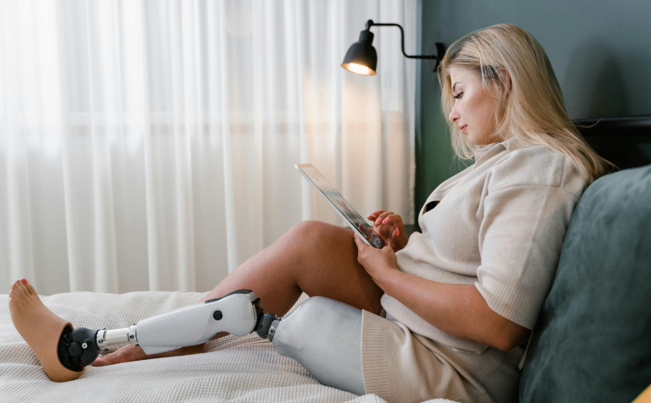 woman with a prosthetic leg sitting in bed while reading. An artificial limb is an eligible medical expense 
