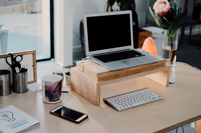 a work from home setup with a laptop on a stand, external keyboard, mobile phone, salt lamp, and flowers on a work desk