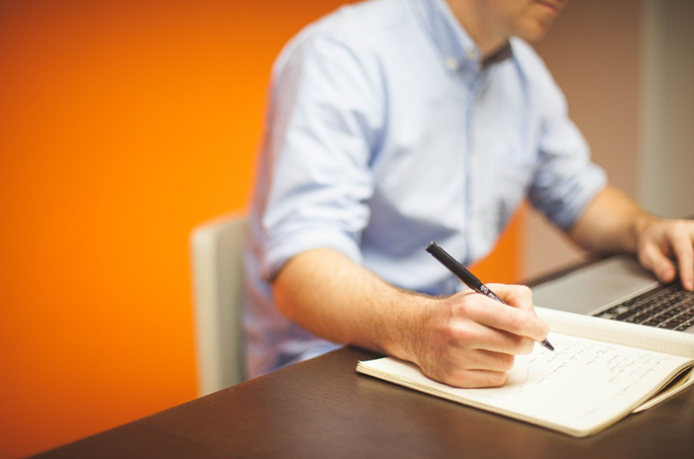 manager at a desk with a laptop, a pen and notebook, taking notes to prepare for a performance review meeting