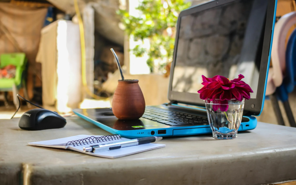 a typical work setup for a digital nomad: a laptop, mouse, a notebook, and a drink in a clay cup amidst a rustic setting