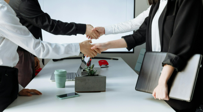 Four professionals in business attire shaking hands across a table after finalizing an NDA 