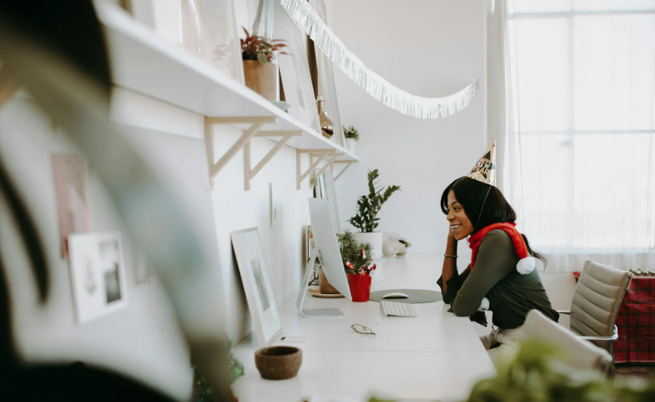 Woman alone at her desk, wearing a party hat while speaking to someone on the Achievers platform 