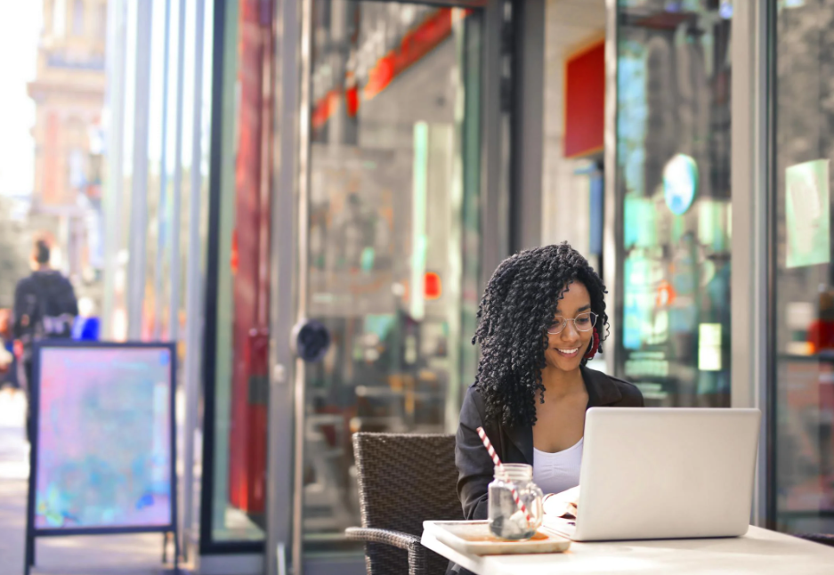 a woman works at her laptop at an outdoor cafe in a foreign country, which her company’s remote work policy allows 