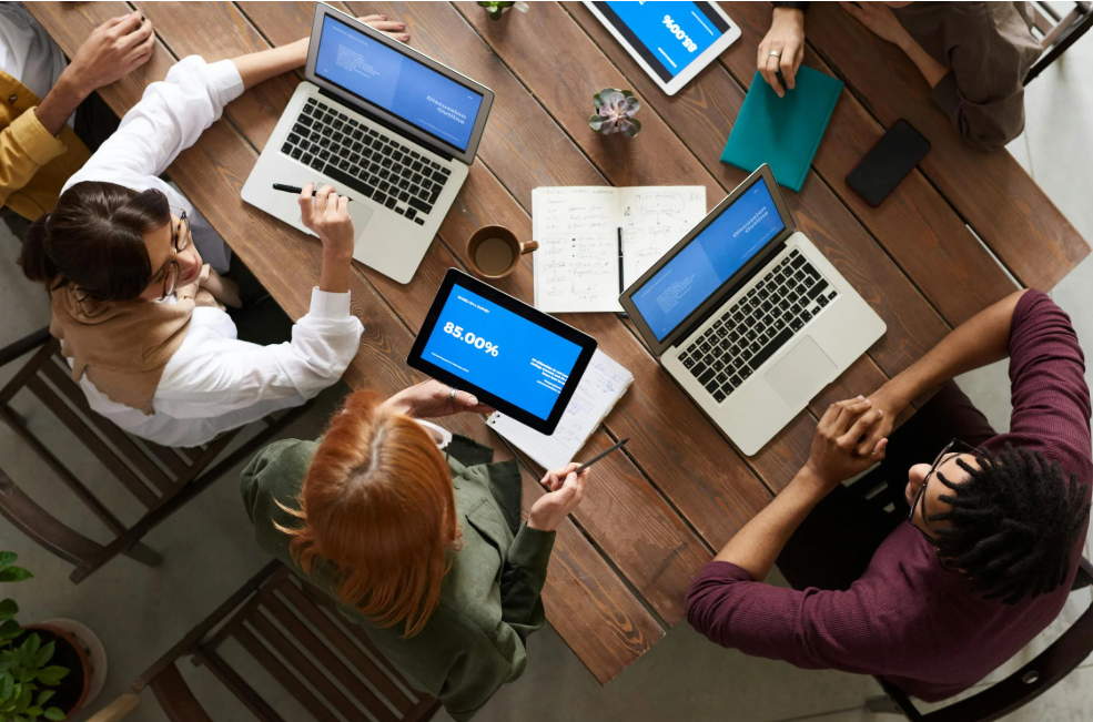 a working group made up of IT, legal, team leads, and HR are at a table with their laptops, drafting a remote work policy 
