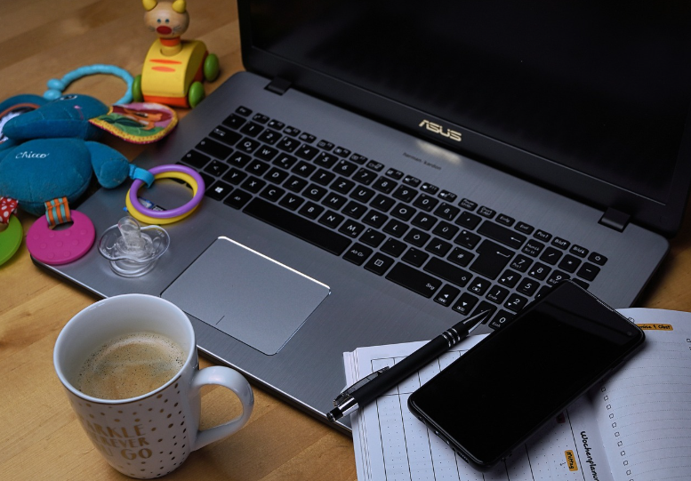 a tabletop showing a laptop, mobile phone, a cup of coffee, and a toddler’s toys: what work-life balance could look like