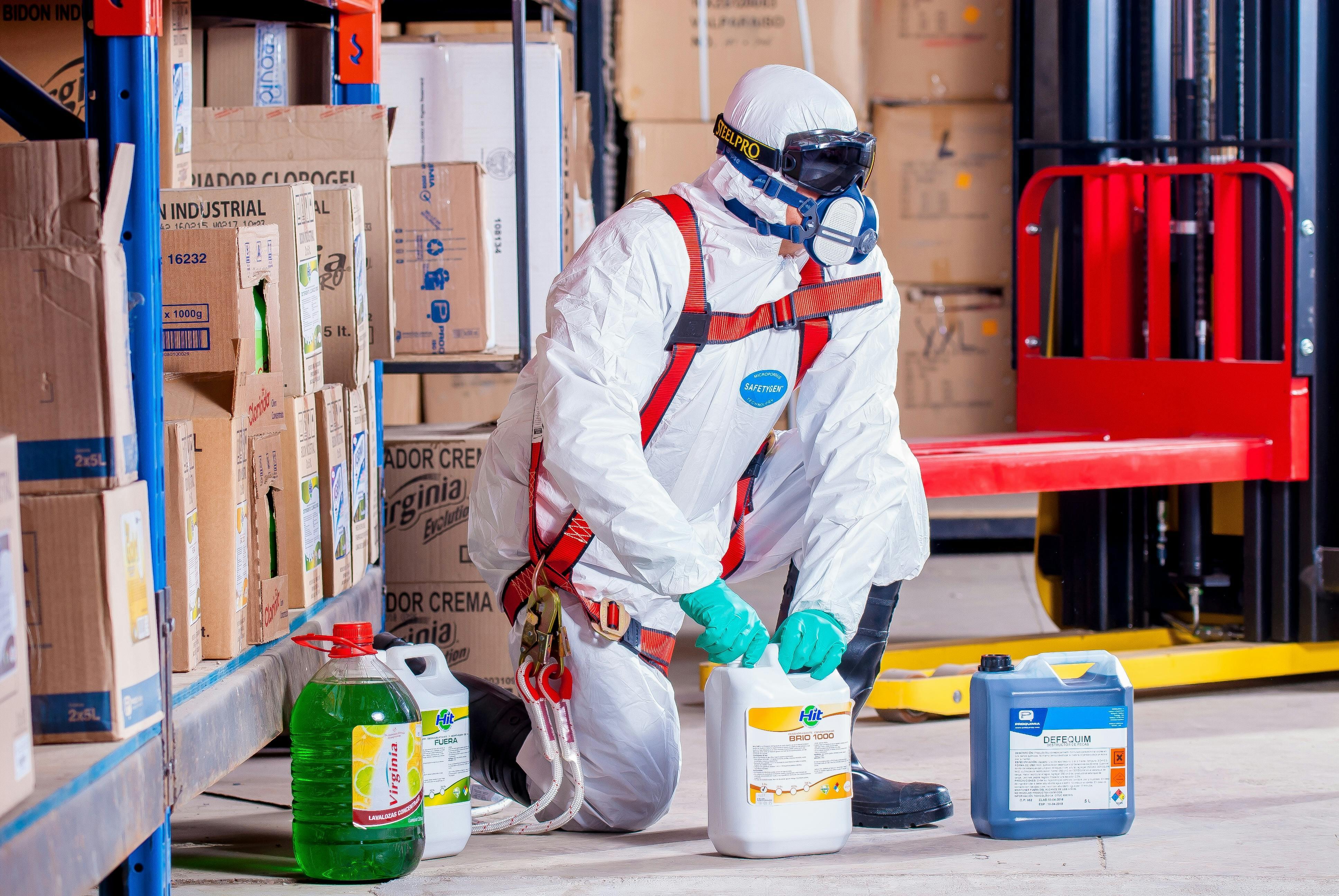  worker in full protective suit wearing goggles and protective mask while handling jars of chemicals