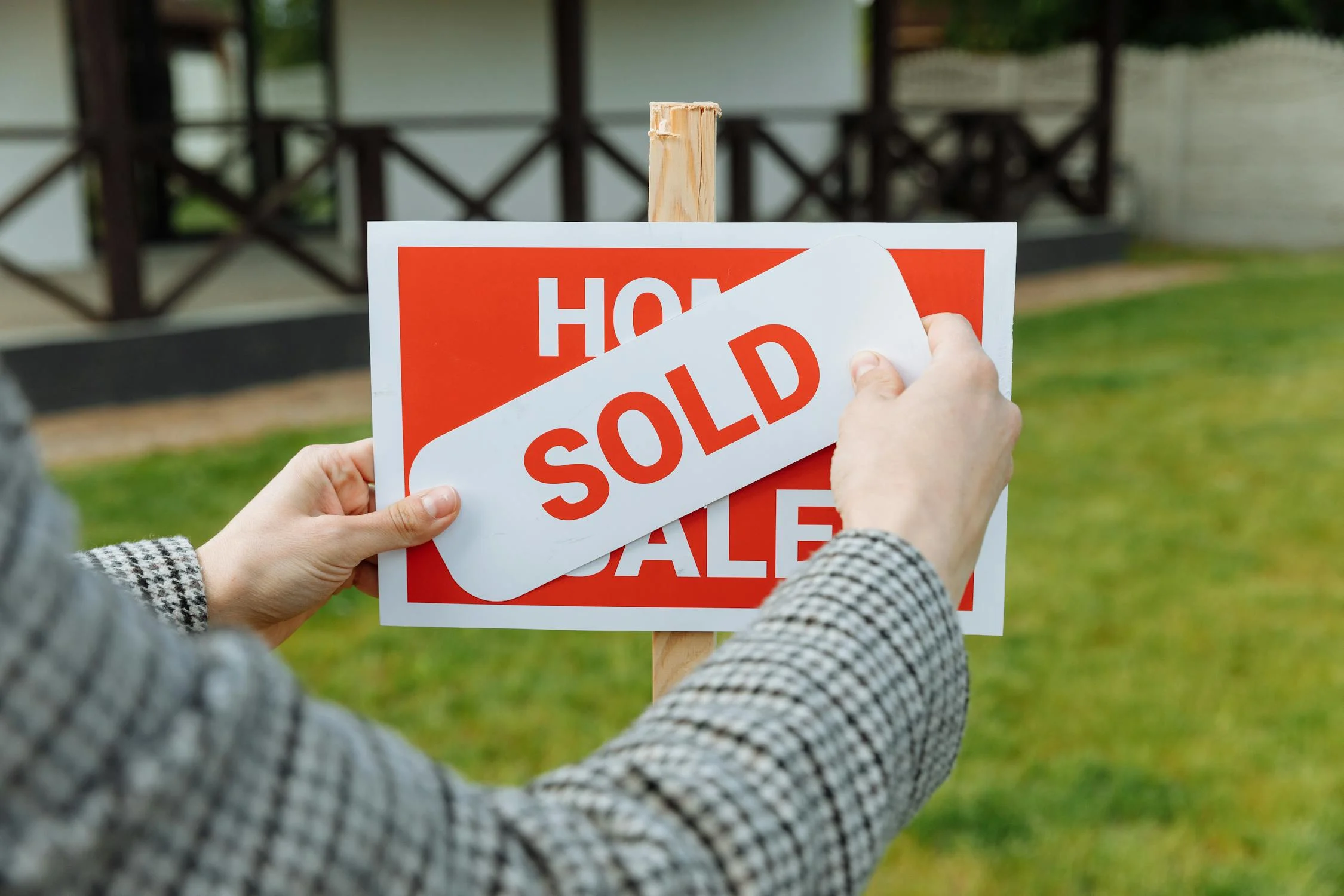 a “sold” sticker is covered over a "house for sale” sign