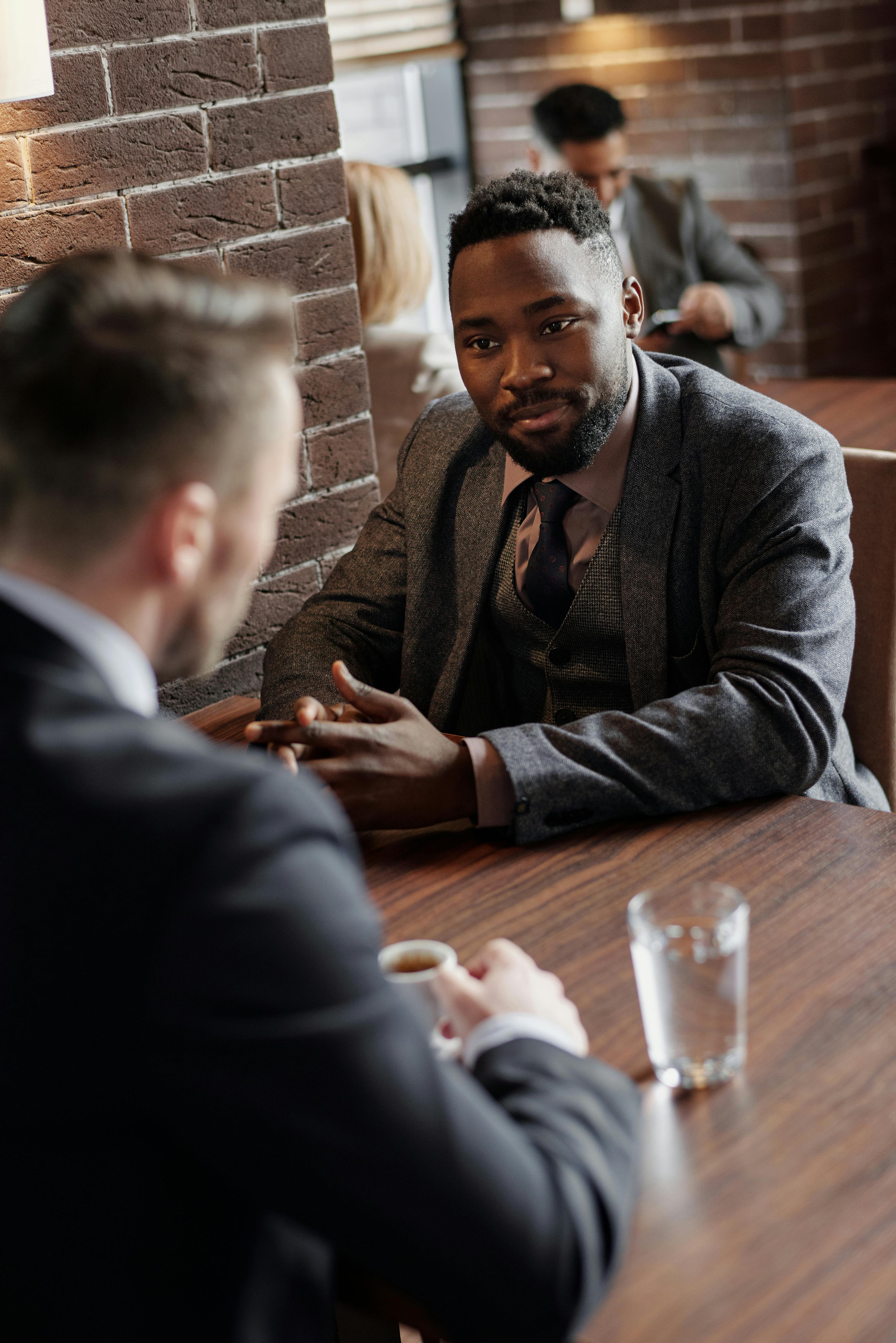 Black man in a suit, listening intently to a man sitting across him at a table