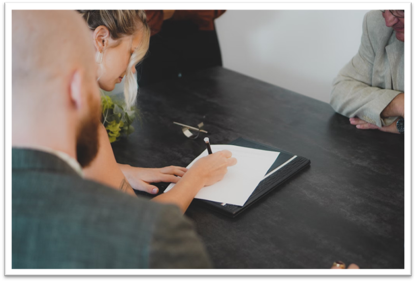 a female homebuyer signing a rental contract on black wooden table with her mortgage broker and landowners present