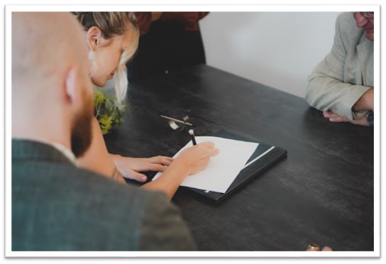 a female homebuyer signing a rental contract on black wooden table with her mortgage broker and landowners present 