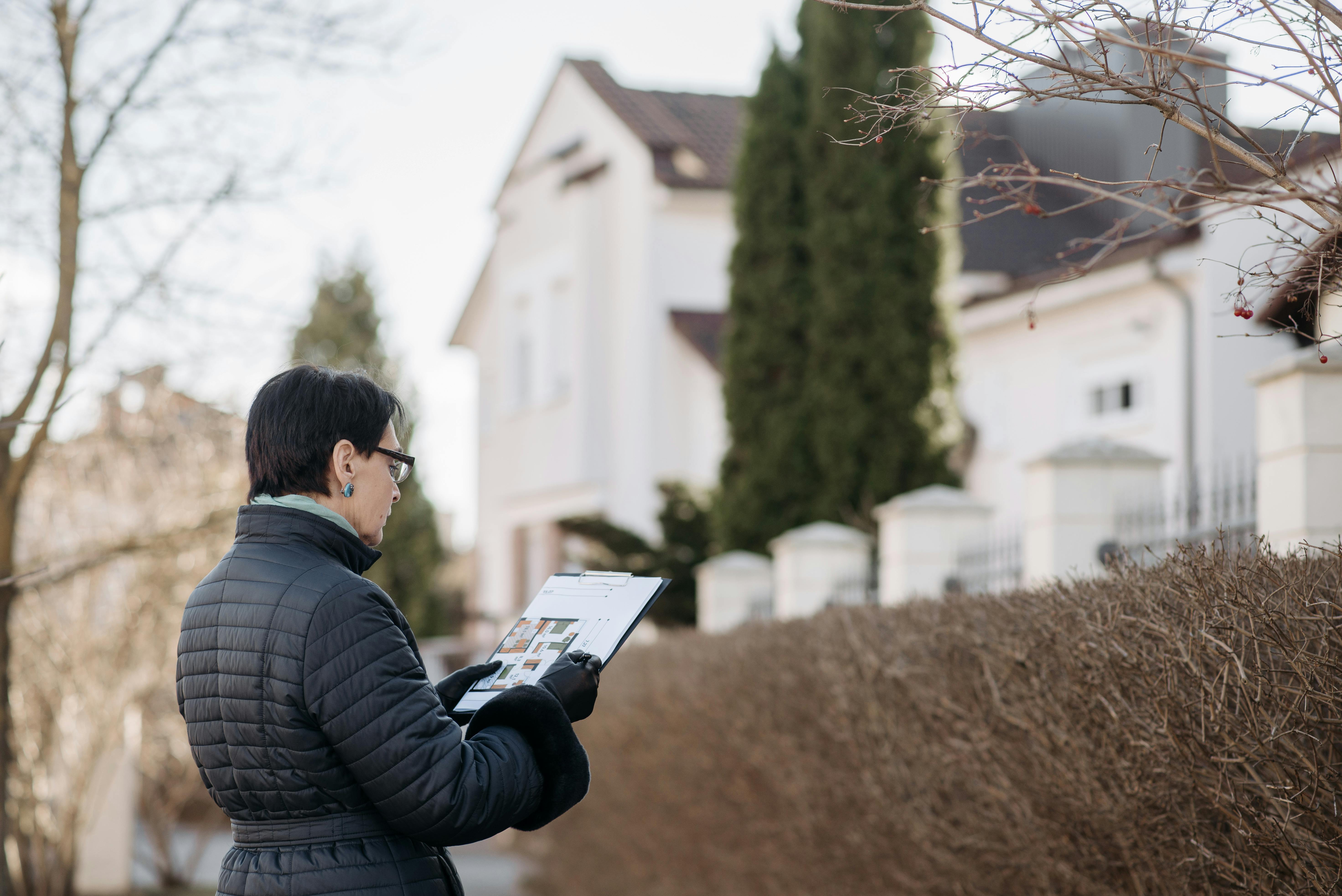  A female real estate agent in a black jacket is looking at a house plan outside a home