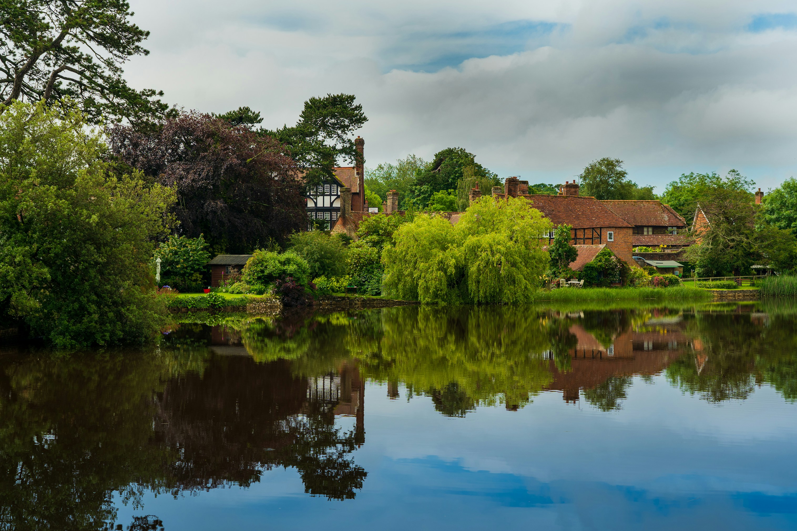 a brick house and trees reflected on a lake in Beaulieu, New Forest