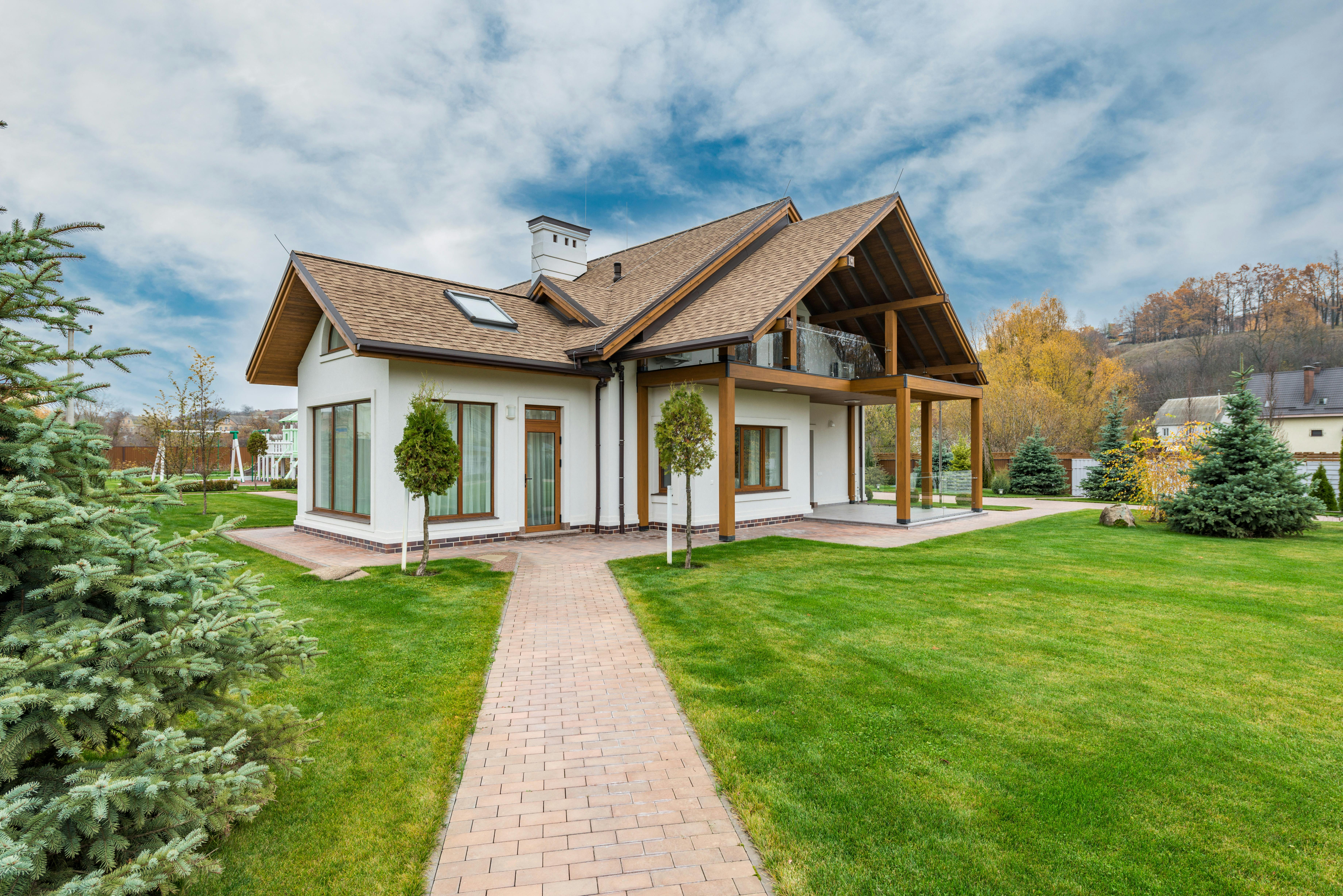  cottage with a brick path leading to it, a mowed lawn in front, and trimmed trees and bushes all around