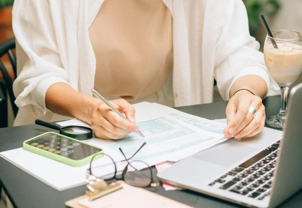 a home buyer in the United Kingdom is assessing her finances using her phone’s calculator and laptop to prepare for her mortgage application costs